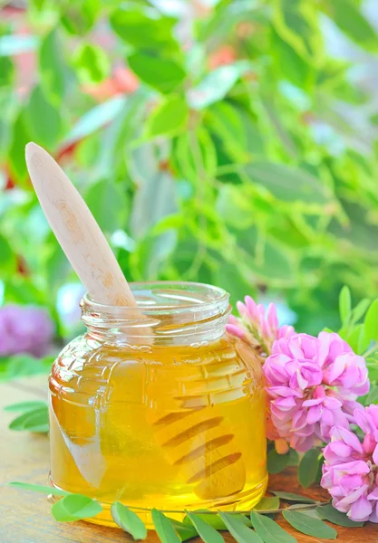 Frasco de vidro cheio de mel e pau com acácia rosa e branco flo — Fotografia de Stock