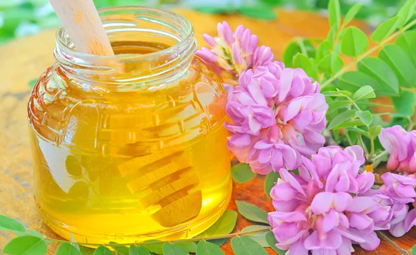 Pot en verre plein de miel et bâton avec rose acacia et flo blanc — Photo