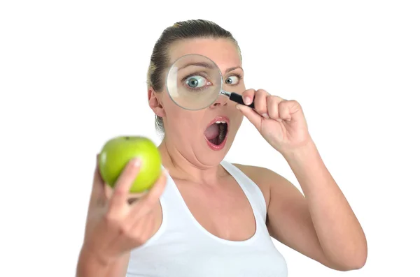 Gesunde blonde glückliche Frau beobachtet grünen Apfel mit einer Lupe — Stockfoto