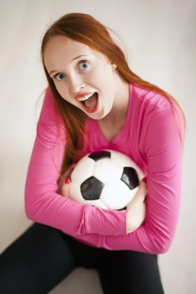 Attraktives blondes Mädchen, das einen Fußball hält und auf dem Boden sitzt — Stockfoto