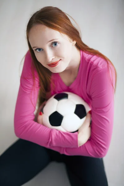 Atrakcyjny blond dziewczynka trzymając piłki nożnej i siedzi na podłodze — Zdjęcie stockowe