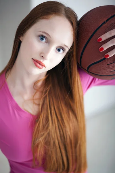 Hermosa chica de pelo largo sosteniendo una pelota de canasta y mirándonos — Foto de Stock