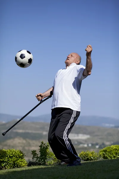 Un futbolista senior con bastón jugando una pelota de fútbol —  Fotos de Stock