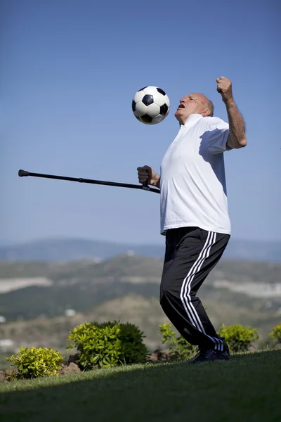 Un futbolista senior con bastón para encabezar una pelota de fútbol — Foto de Stock