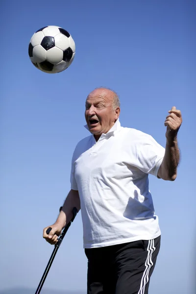 Ein älterer Fußballspieler mit Gehstock, um einen Fußballball zu köpfen — Stockfoto
