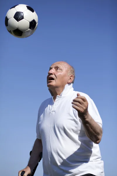Un futbolista senior con bastón para encabezar una pelota de fútbol —  Fotos de Stock