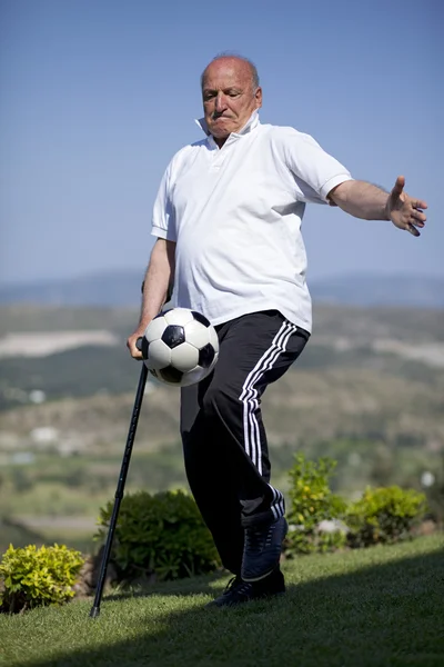 Un futbolista senior con bastón jugando una pelota de fútbol —  Fotos de Stock