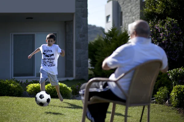 Großvater sitzt auf Stuhl und sein Enkel spielt Fußball — Stockfoto