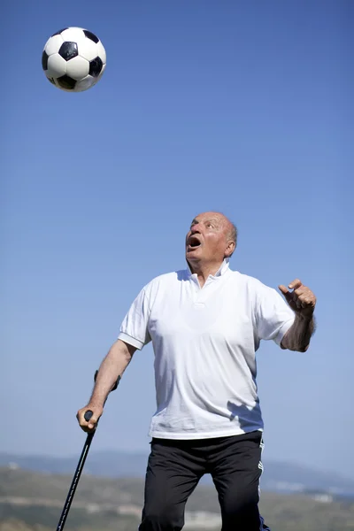 Um jogador de futebol sênior com bengala para liderar uma bola de futebol — Fotografia de Stock