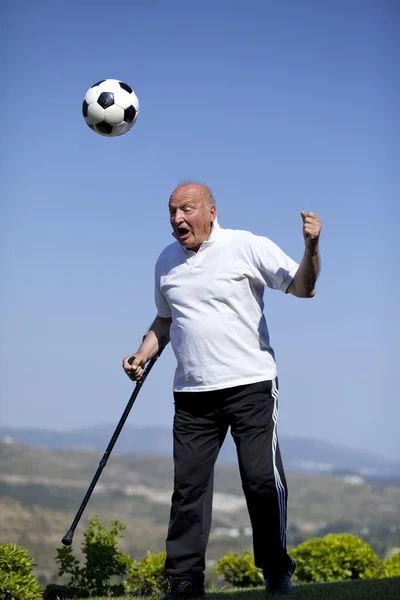 Un futbolista senior con bastón para encabezar una pelota de fútbol — Foto de Stock