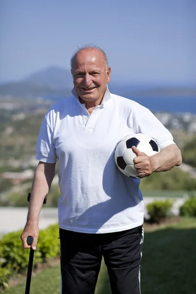 Un futbolista senior con bastón sosteniendo una pelota de fútbol —  Fotos de Stock