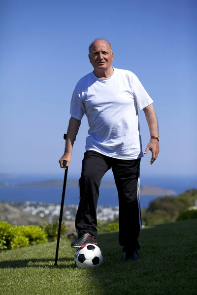 Un giocatore di calcio anziano con bastone da passeggio in possesso di un pallone da calcio — Foto Stock