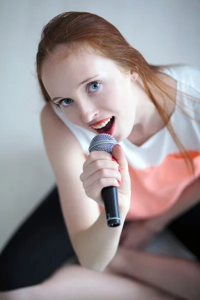 Рыжая молодая женщина держит микрофон и сидит — стоковое фото