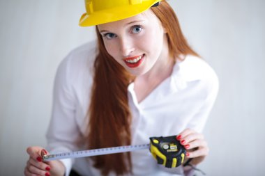 Young beautiful female with yellow helmet holding a tape measure clipart