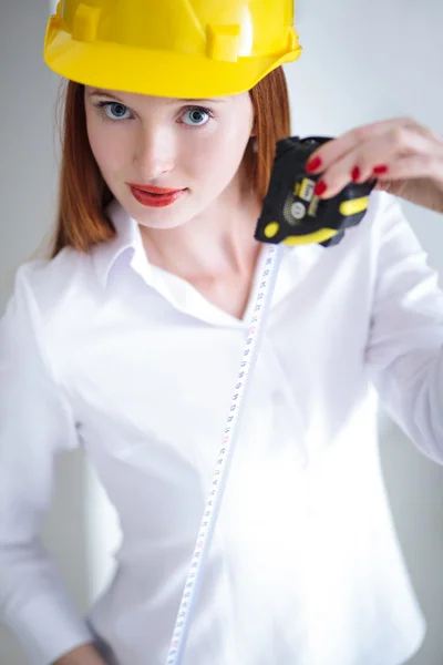 Joven hermosa hembra con casco amarillo sosteniendo una cinta métrica — Foto de Stock