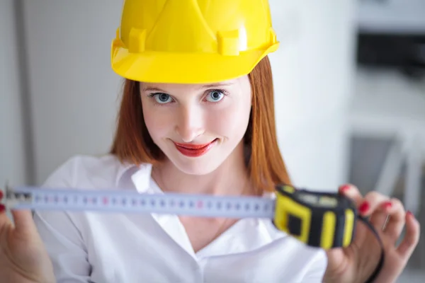 Young beautiful female with yellow helmet holding a tape measure — Stock Photo, Image