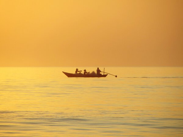 Fishing boat with net and 3 on board sets out to the fishing grounds as the sun sets