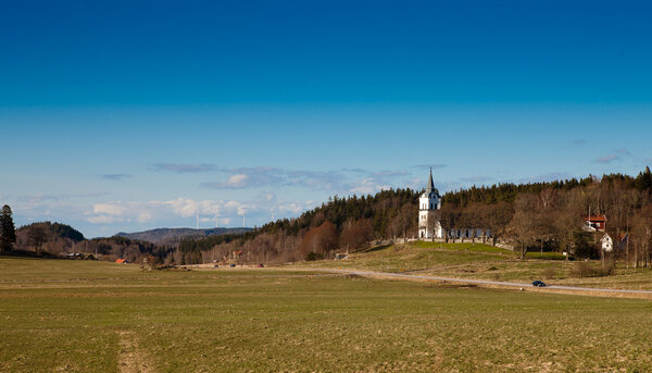 An idyllic view of the swedish countryside. An old church and some houses, a road and farmland.