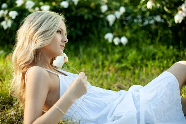 Vacker blond tjej med blomma på gräs, vit klänning — Stockfoto