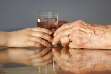 Hands of grandmother and grandchild with the glass of water clipart