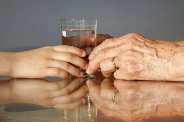 Τα χέρια της γιαγιάς και εγγόνι με το ποτήρι του νερού — Φωτογραφία Αρχείου
