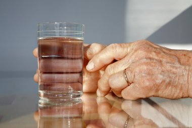 Hands of old woman and glass of water clipart