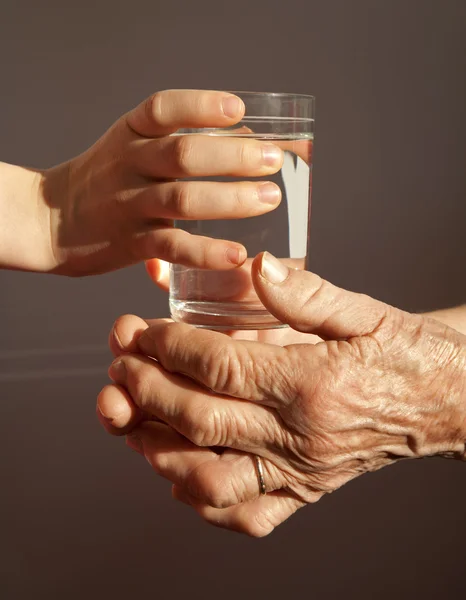 Mani di nonna e nipote con il bicchiere d'acqua — Foto Stock