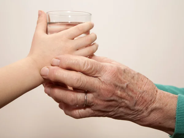 Mains de grand-mère et petit-enfant avec le verre d'eau — Photo
