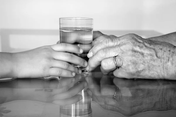 Руки бабушки и внука со стаканом воды — стоковое фото
