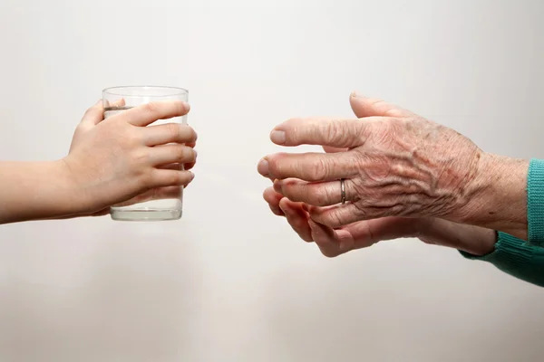 Handen van grootmoeder en kleinkind met het glas water — Stockfoto