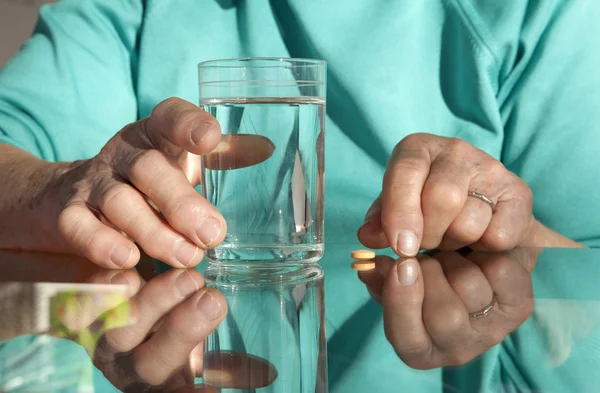 Manos de anciana con una pastilla y agua — Foto de Stock