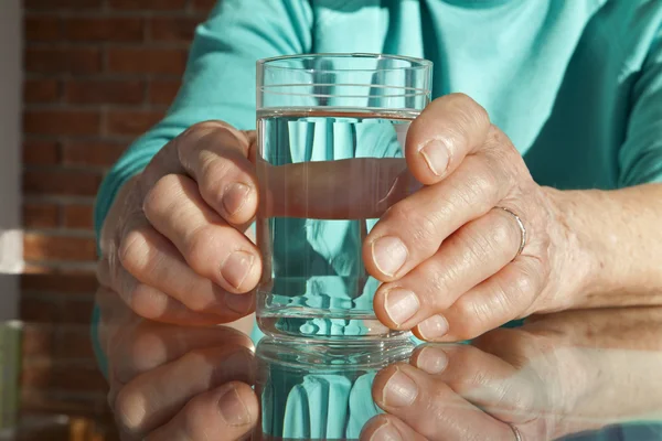 Hands of old woman and glass of water — Stock Photo, Image