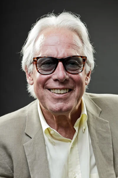 Lächelnder älterer Herr im Anzug mit Sonnenbrille auf grauem Hintergrund. — Stockfoto