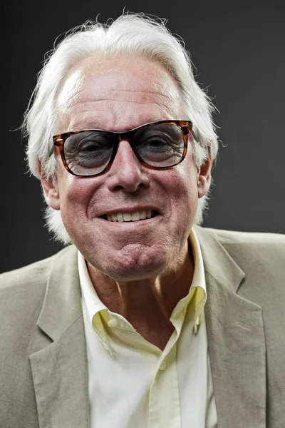 Uśmiechający się starszy człowiek w garniturze sobie okulary na białym tle na szarym tle. — Zdjęcie stockowe