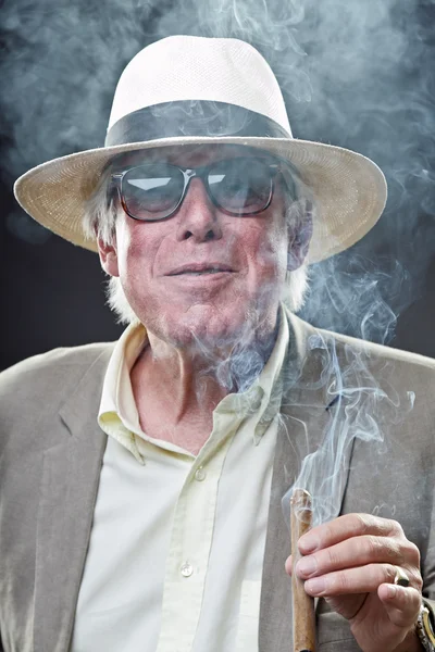 Homme âgé avec chapeau et lunettes de soleil fumant cigare . — Photo
