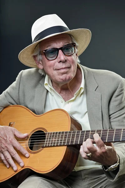 Starší muž s kloboukem a sluneční brýle, hraje akustická kytara. — Stock fotografie