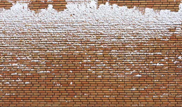 Frozen orange brick wall covered with snow