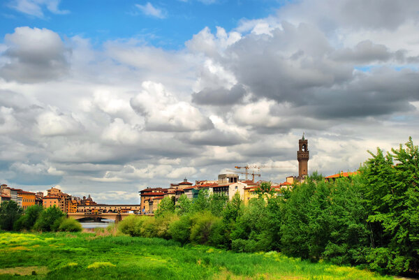 Beautiful view of Flornce, Arno River and famous Old Bridge (Ponte Vecchio) and majestic powerful clouds. Vivid meadow near the river.