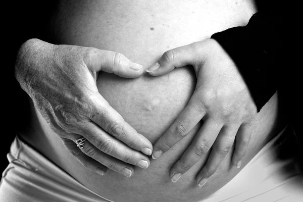 Старая и молодая рука на беременном животе — стоковое фото