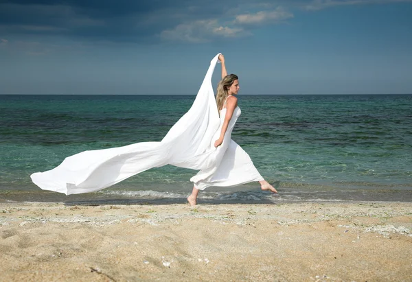 Mujer rubia delgada corre en la playa, con chal blanco — Foto de Stock