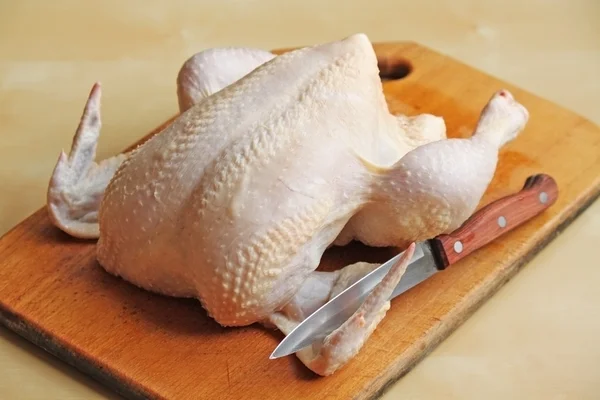 Целый сырой цыпленок на доске с ножом — стоковое фото