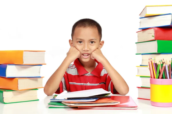 Petit garçon avec ses devoirs, avec beaucoup de livres autour de lui — Photo