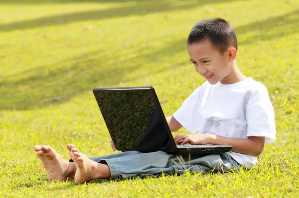 Heureux petit garçon jouer ordinateur portable sur l'herbe — Photo