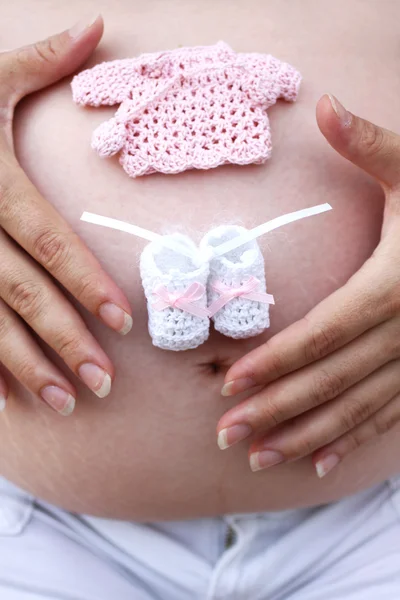 stock image Pregnant woman with baby socks and sweater on belly.