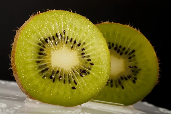 Kiwifrukt doppade i svart bakgrund på disken — Stockfoto