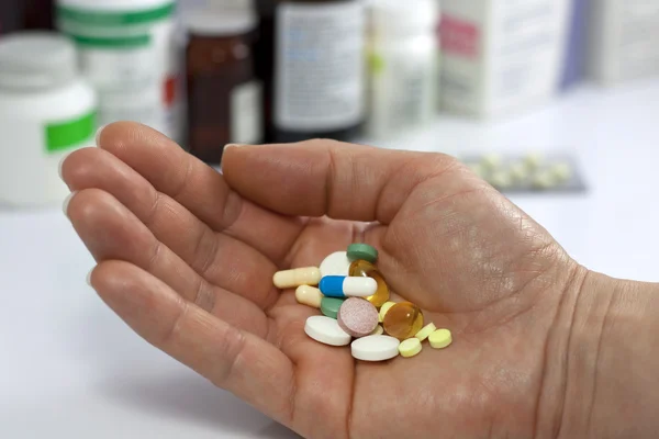 Таблетки в руке против лекарств в аптеке — стоковое фото