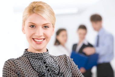 Portrait of blonde businesswoman looking at camera in working environment clipart