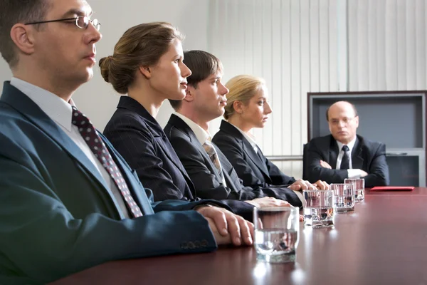 Gespannen jonge zitten aan de tafel in een lijn en hun ontevreden baas — Stockfoto