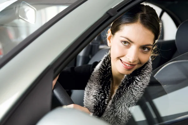 Porträt einer lebhaften Brünetten, die interessiert durch das Fenster ihres Autos blickt — Stockfoto