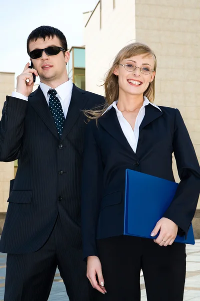 Retrato de empresária bem sucedida segurando pasta azul com seu parceiro em segundo plano — Fotografia de Stock